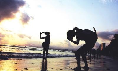 三亚湾海边，夕阳斜照，两名年轻的女孩兴奋地在海滩上拍照，留下青春靓影。袁永东